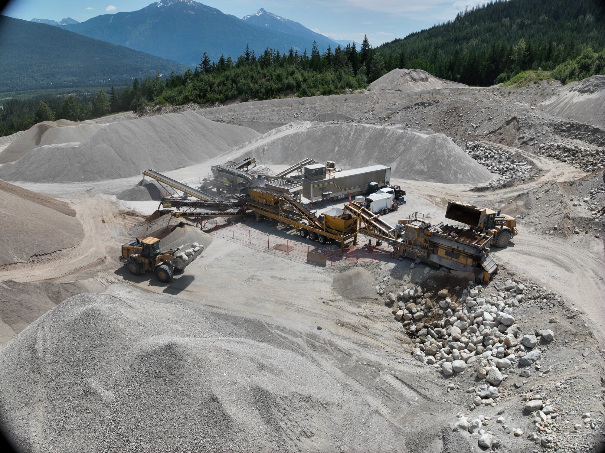 A Cantex mobile crushing spread set up on a pit floor with stockpiles around it and snow-topped mountains on the horizon.