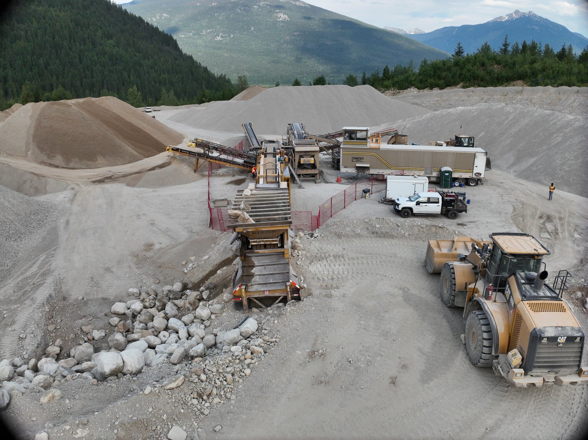 A Cantex crushing spread and its stockpiles on a pit floor, with a forested ridge and mountains behind.