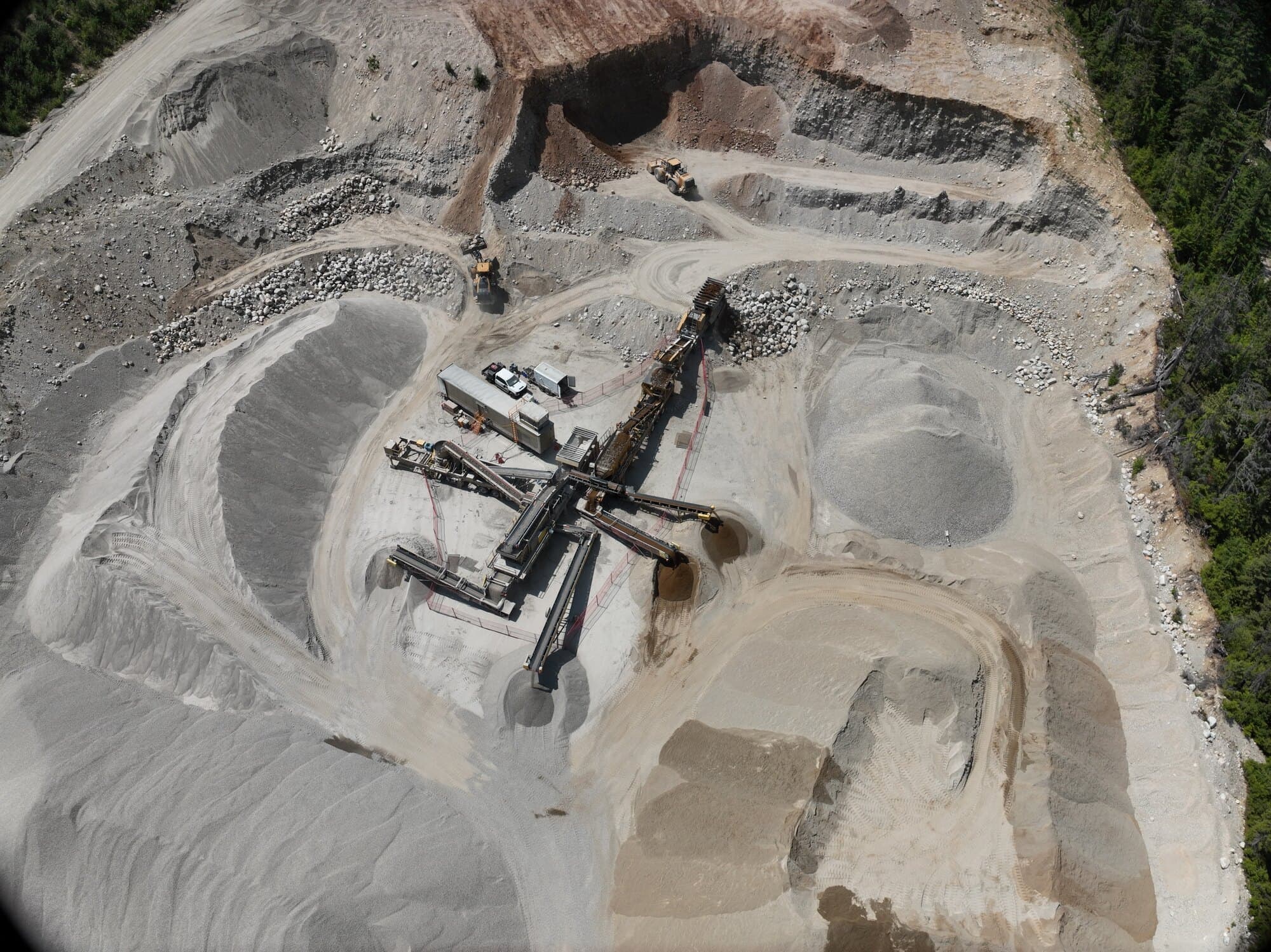 A straight-down drone view of a Cantex crushing and screening spread, with finished stockpiles fanned out around it inside a forested pit.
