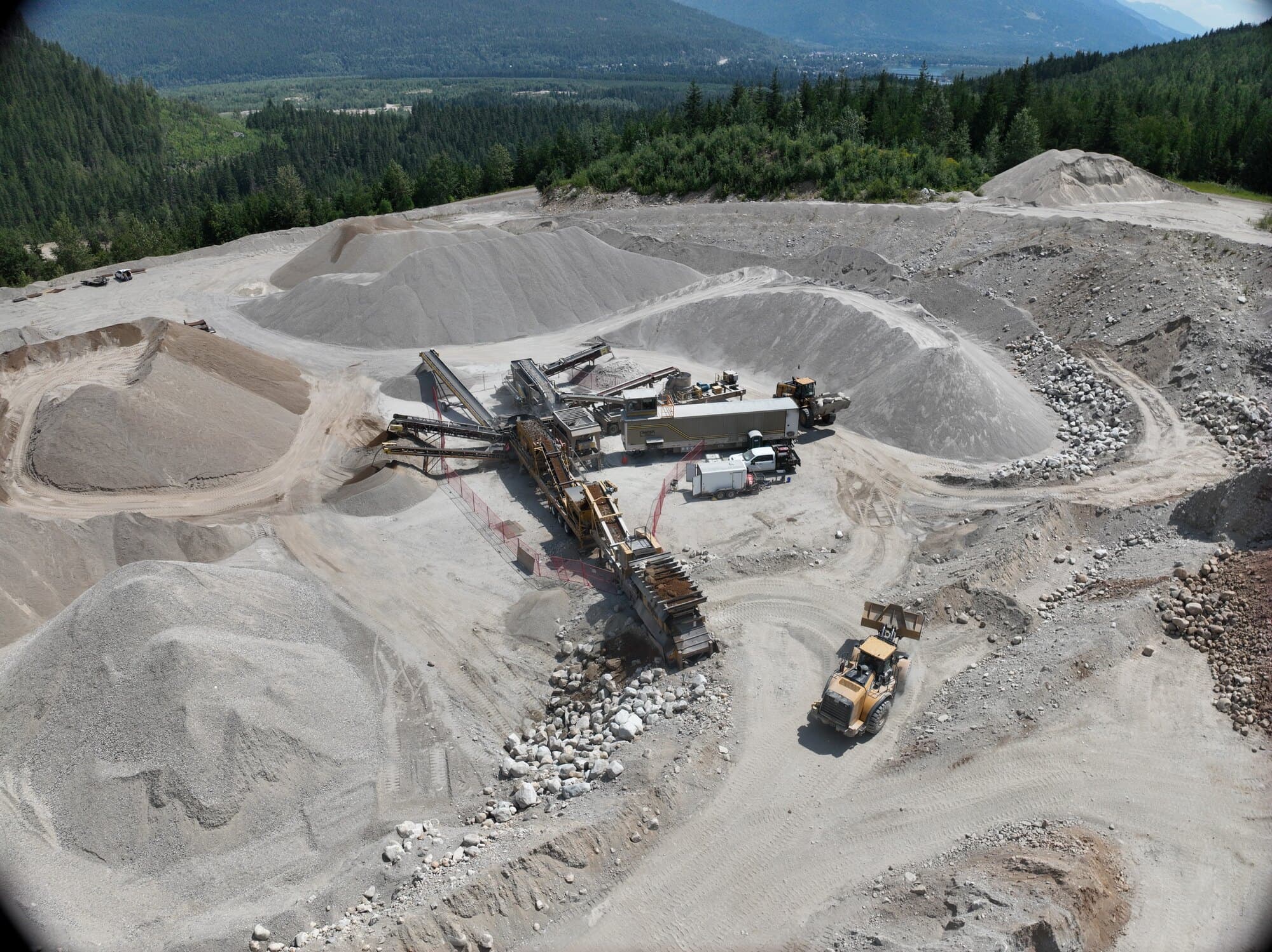 A drone view of a Cantex crushing spread working stockpiles on a bench, with a forested valley and lake in the distance.