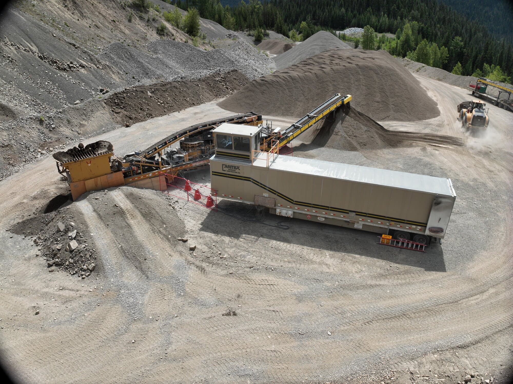 A Cantex crushing plant being fed at the jaw while a stacking conveyor builds a stockpile behind it, seen from the air.