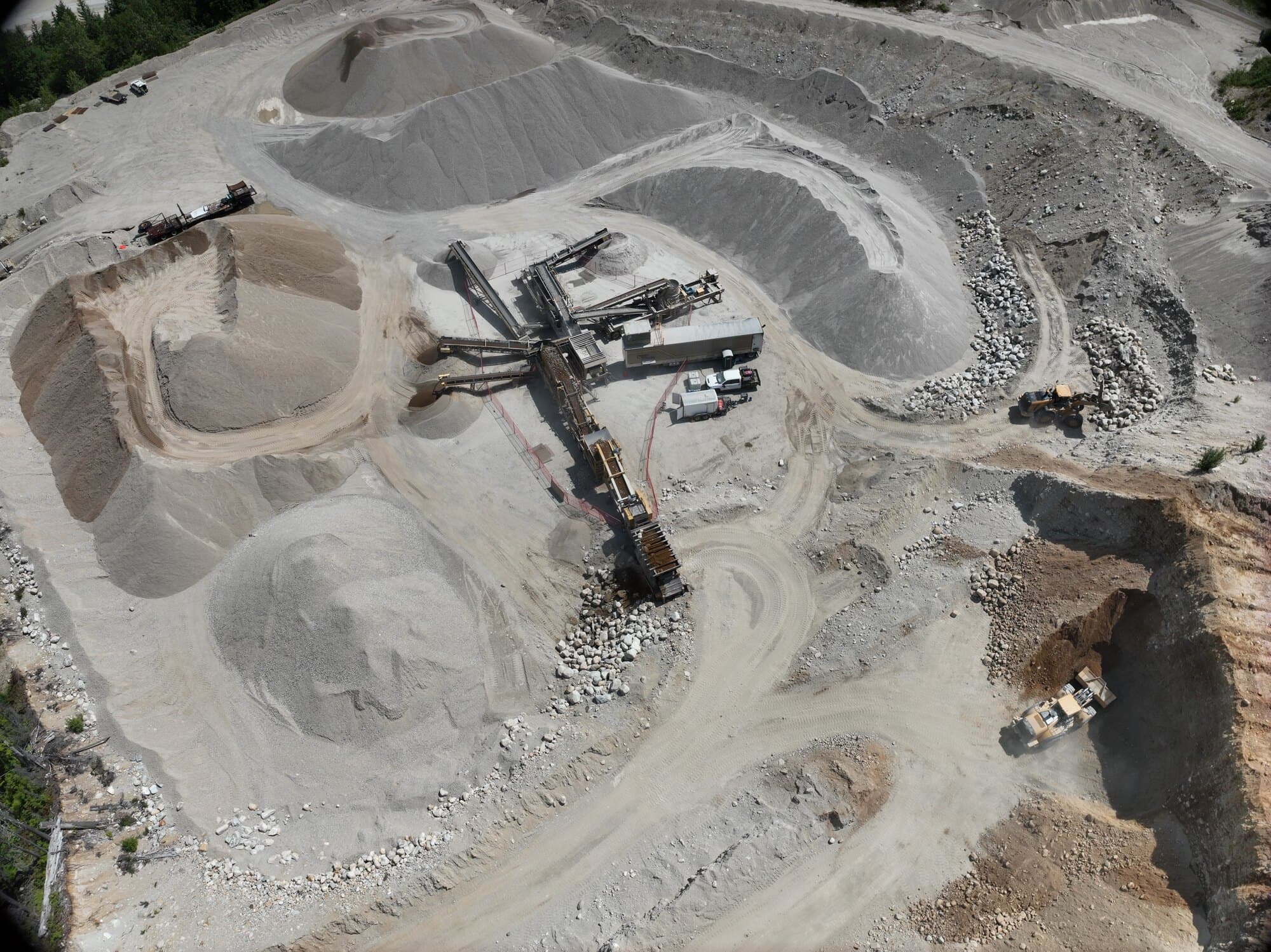 A straight-down drone view of a working pit: terraced benches, haul roads, and separated stockpiles of finished product around a crushing spread.