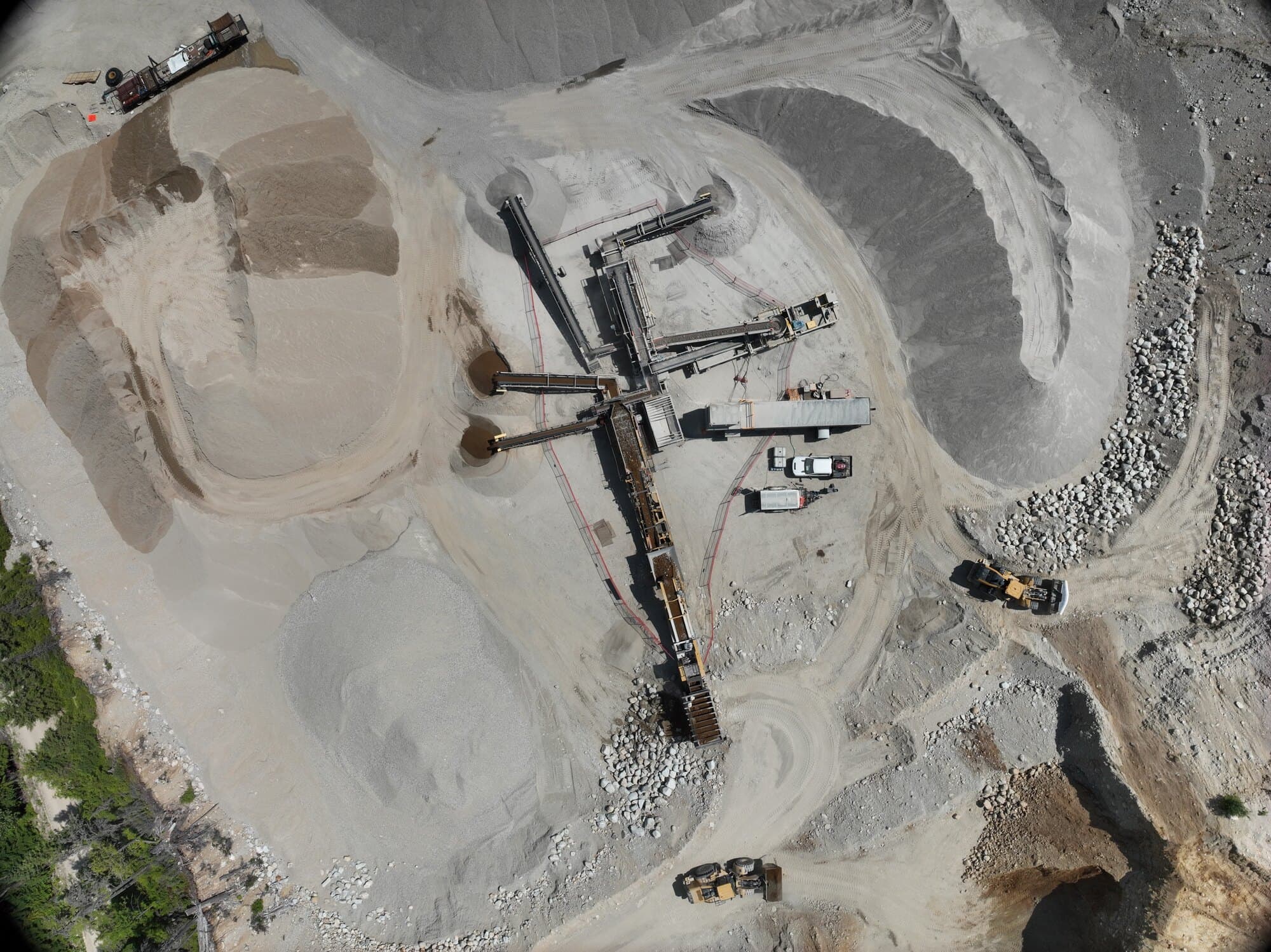 A straight-down drone view of a crushing and screening plant with its stacking conveyors fanned out into separate product piles.