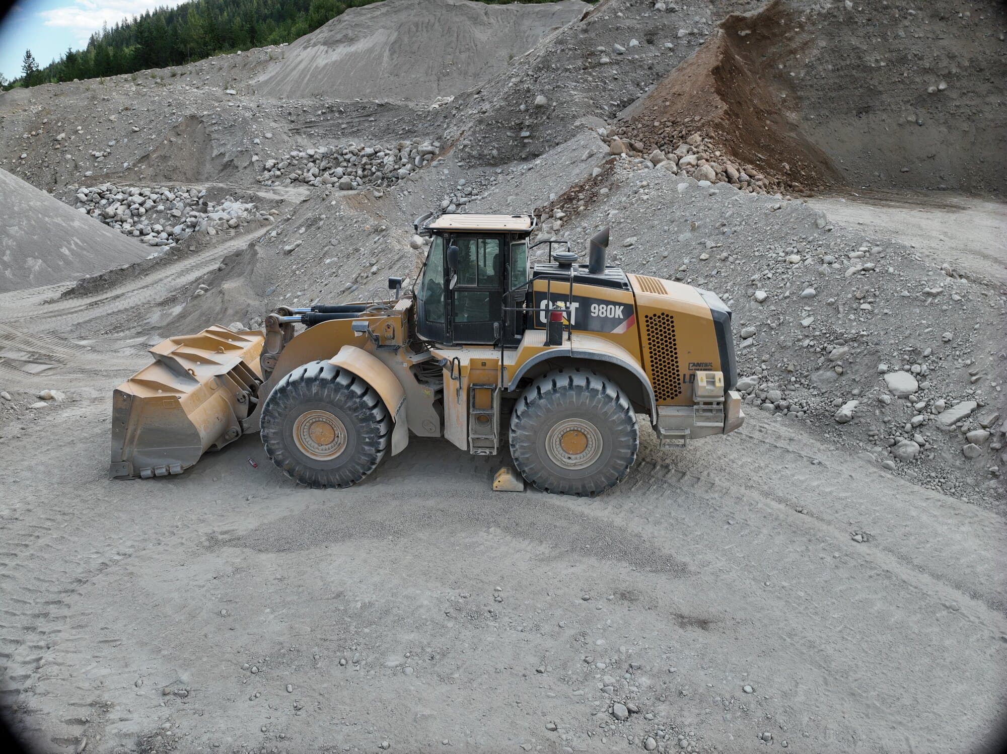 A Cat 980K wheel loader working the floor of a pit beside blasted rock and a stripped bench.
