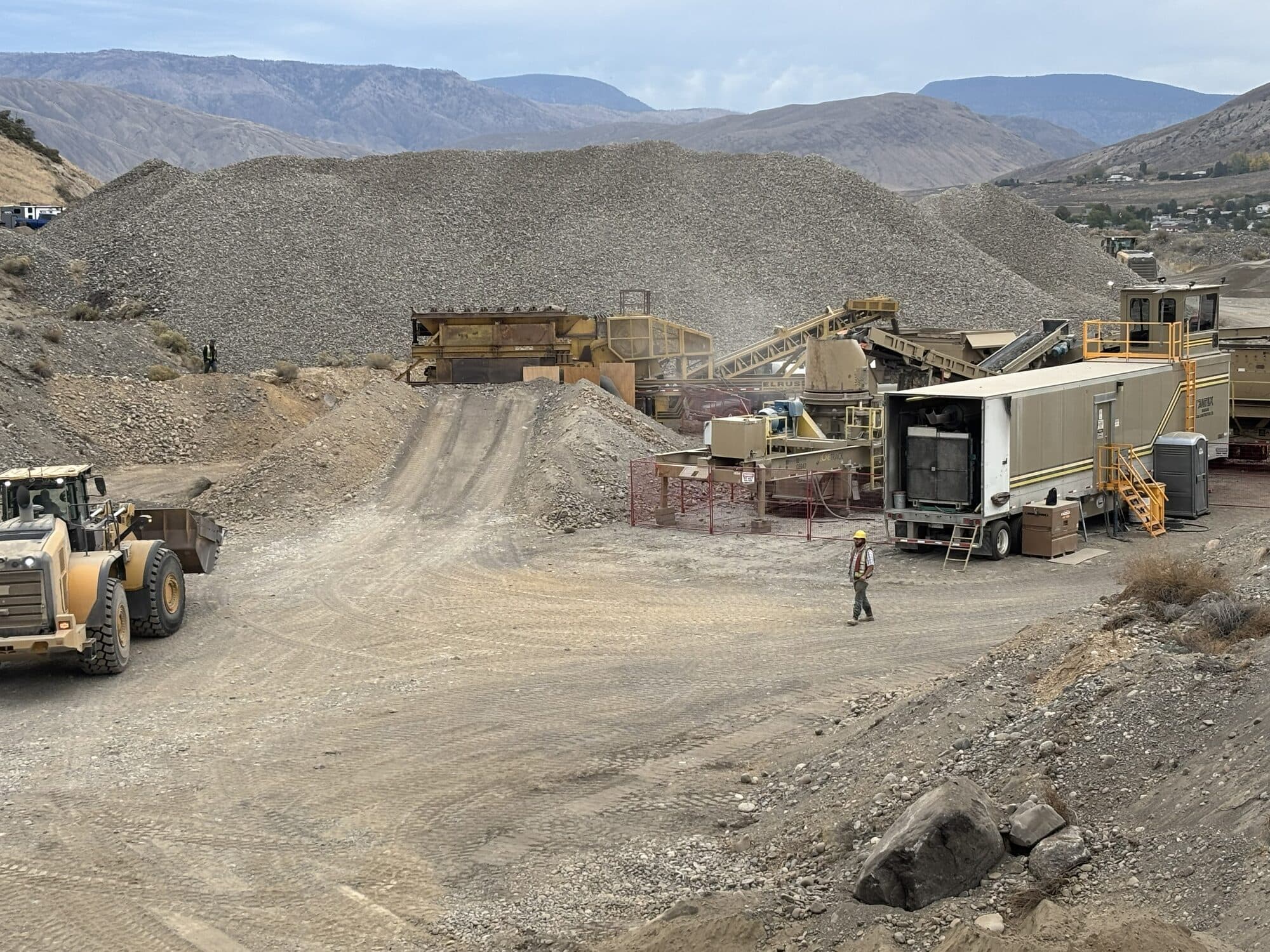 A Cantex crushing spread with a wheel loader and an operator moving stockpiles, mountains in the distance.