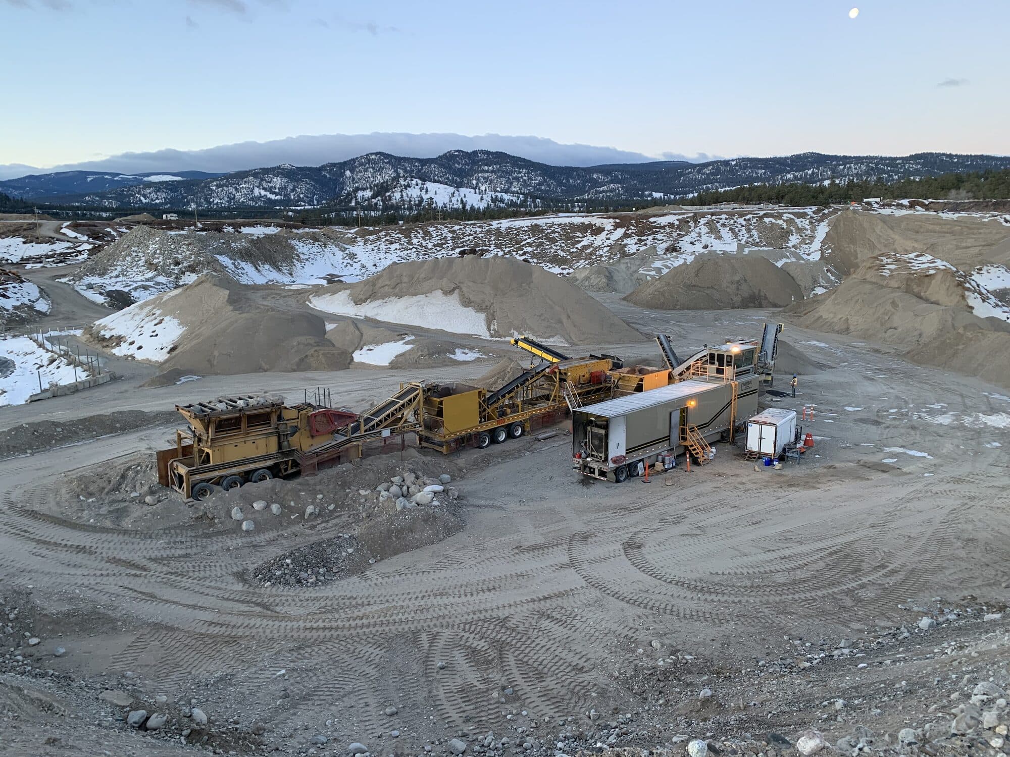 A Cantex mobile crushing spread set up on a remote site at dusk, snow on the ground and mountains behind.