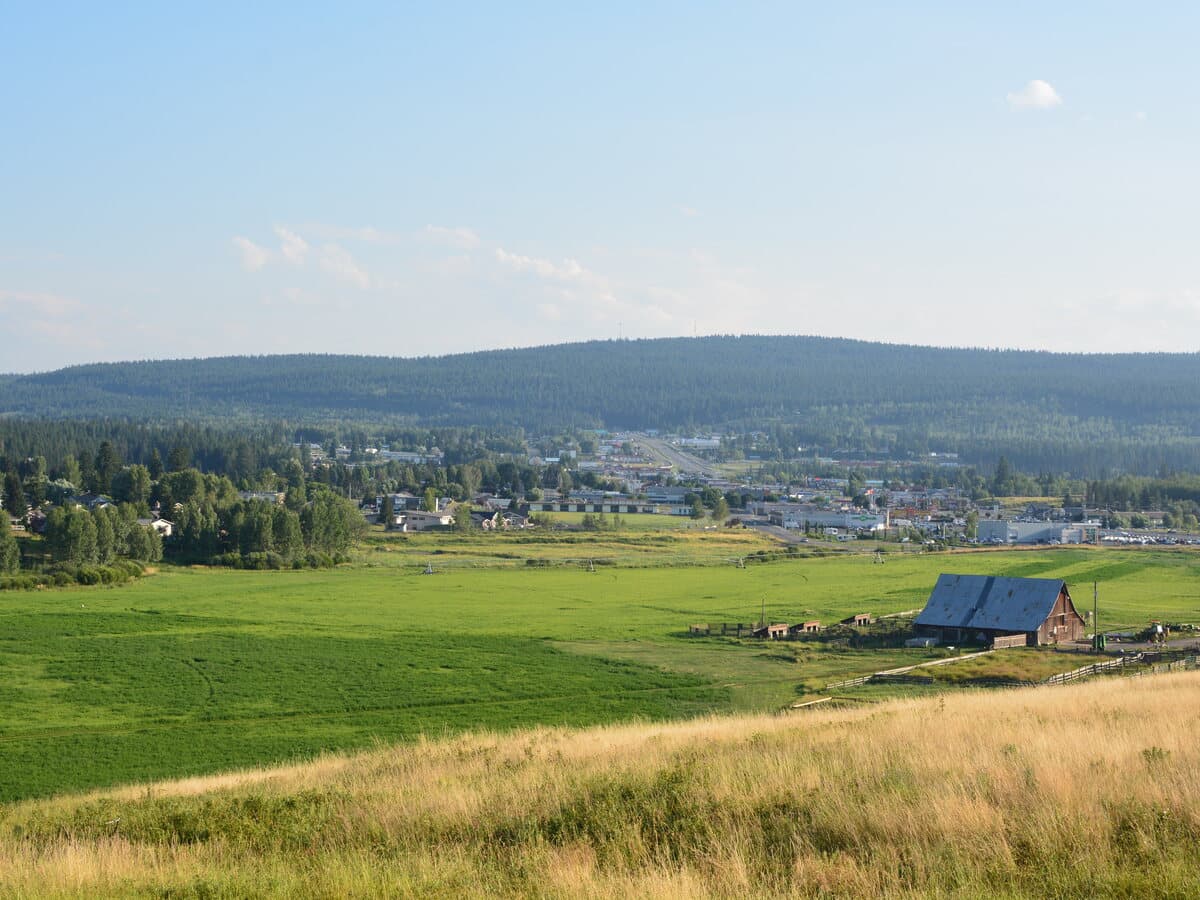 A view across open Cariboo ranchland toward the town of 100 Mile House and the forested ridges beyond.